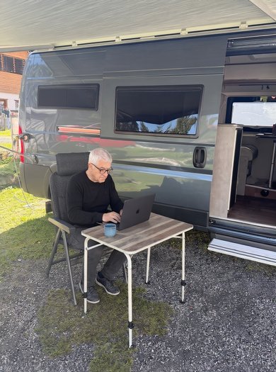 Walter Uehli schreibt am Laptop vor seinem Pössl-Wohnmobil